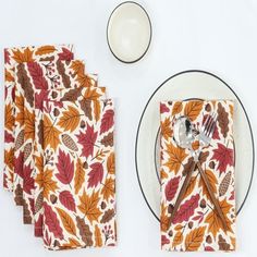 the place setting is ready to be served on the white tablecloth with autumn leaves