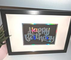 a happy birthday sign is displayed in a black frame on a table next to a potted plant