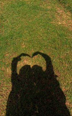 the shadow of a person's hand on grass with a frisbee in the shape of a heart