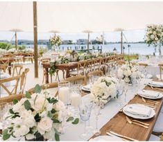 a table set up with white flowers and candles for an outdoor wedding reception by the water