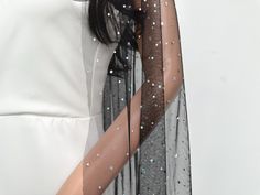 a woman wearing a white top and black scarf with silver sequins on it