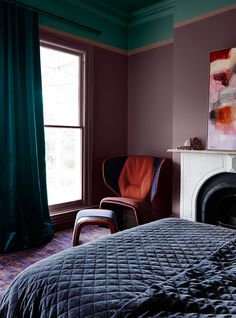 a bedroom with a bed, chair and painting on the wall next to a fireplace