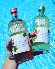 someone holding two bottles of absolut hawberry next to a swimming pool