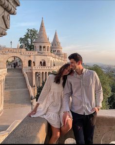 a man and woman standing next to each other in front of a castle