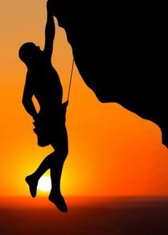 a man climbing up the side of a mountain at sunset