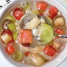 a white bowl filled with fruit and vegetables next to a spoon on top of a table