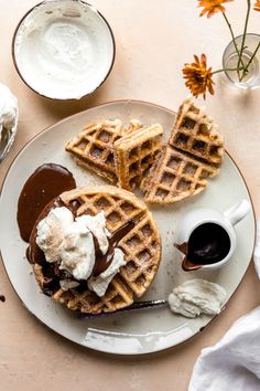 waffles with ice cream and chocolate sauce on a white plate next to flowers