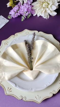 a white plate topped with a flower next to a purple table cloth