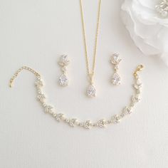 a necklace, bracelet and earring set on a white surface with flowers in the background