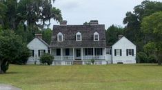 a large white house sitting in the middle of a lush green field next to trees