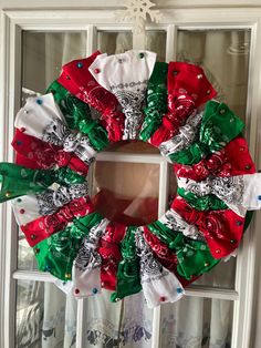 a christmas wreath hanging on the side of a window with red, green and white ribbons