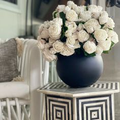 a black vase filled with white flowers sitting on top of a table next to a chair