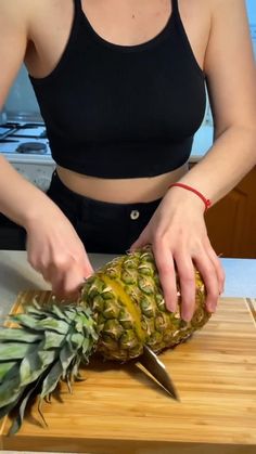 a woman cutting up a pineapple on top of a wooden cutting board with a knife