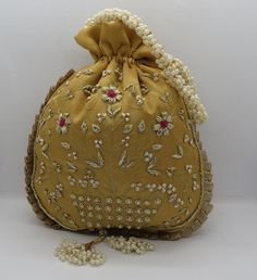 a gold purse with pearls and beads on the bottom is sitting against a white wall