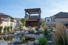 a small pond in the middle of a yard with rocks and plants around it, next to a wooden gazebo