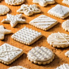 many different types of cookies on a wooden table with snowflakes and icing