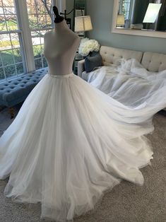 a white wedding dress is on display in a living room with a couch and large windows