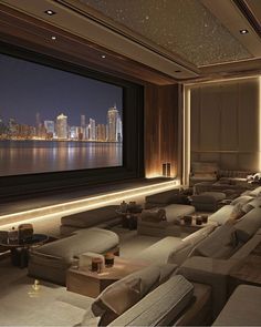 a large screen in a room with couches and pillows on the floor, overlooking a city at night