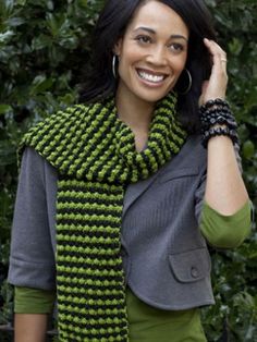 a woman wearing a green and black knitted scarf, smiling at the camera with her hand on her head