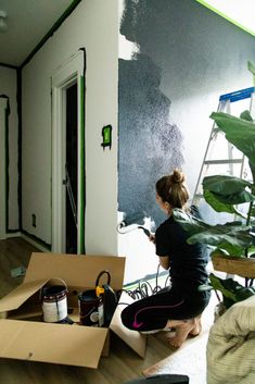 a woman sitting on the floor painting a wall