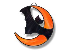 an orange and black bat hanging from the side of a crescent shaped glass ornament