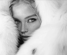 a black and white photo of a woman with fur coat over her head, looking directly into the camera