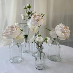 three clear vases with flowers in them on a white table cloth covered tablecloth