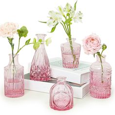 pink glass vases with flowers in them on top of a white box and two books