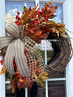 a wreath with fall leaves and berries hanging from the front door, in front of a window