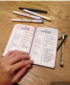 a person is holding a pen and looking at a planner on a wooden table with pens