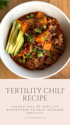 a white bowl filled with chili and avocado on top of a wooden table