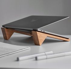 an apple laptop sitting on top of a wooden stand next to a pen and notebook