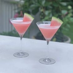 two martini glasses with watermelon garnish sit on a white table outside