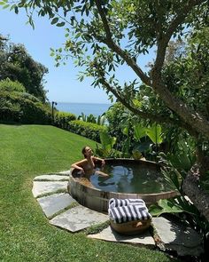 a woman sitting in an outdoor hot tub on top of a lush green field next to the ocean