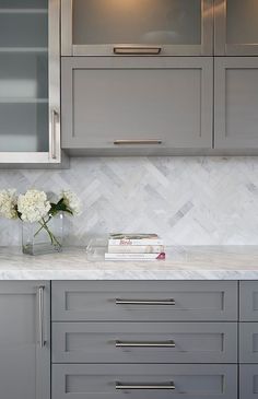 a kitchen with gray cabinets and white marble counter tops, along with flowers in a vase