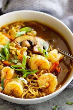 a white bowl filled with noodles and shrimp on top of a gray table next to a napkin