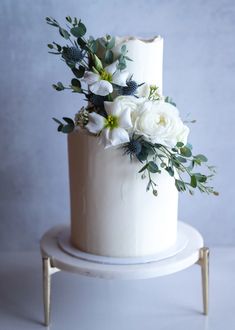 a wedding cake with white flowers and greenery on the top is sitting on a stand