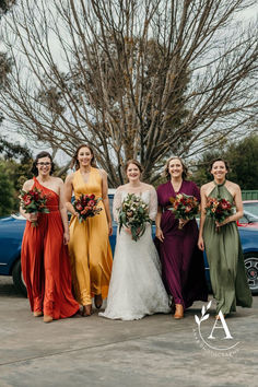 a group of women standing next to each other in front of a blue car and tree