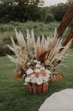 a basket filled with lots of flowers sitting on top of a grass covered field next to a wooden pole