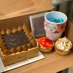 a box filled with cakes and pastries on top of a wooden table next to a cup of coffee