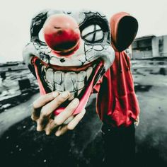 a person wearing a clown mask and holding up a red ball in front of their face