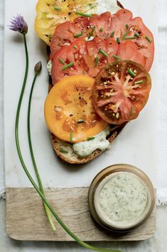 an open face sandwich with tomatoes and cream sauce on a cutting board next to a flower