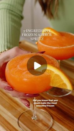 two people holding oranges in their hands and one is holding a wine glass with the word ingredient frozen aperol spritz