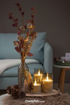 three lit candles sitting on top of a table next to a vase filled with flowers