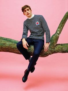 a man sitting on a tree branch wearing a striped shirt and blue pants with black shoes