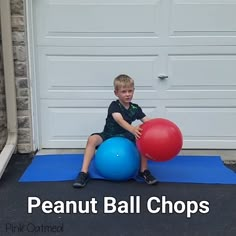 a young boy sitting on top of a blue mat holding two red and one blue balls