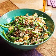 a green bowl filled with food on top of a purple and blue table cloth next to a wooden spoon