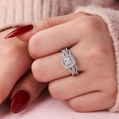 a woman's hand with red nail polish holding a diamond ring on her finger