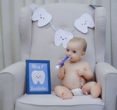 a baby sitting in a chair with a toothbrush in it's mouth next to a sign