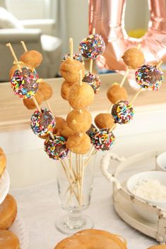 donuts and sprinkles are arranged on sticks in front of a glass vase